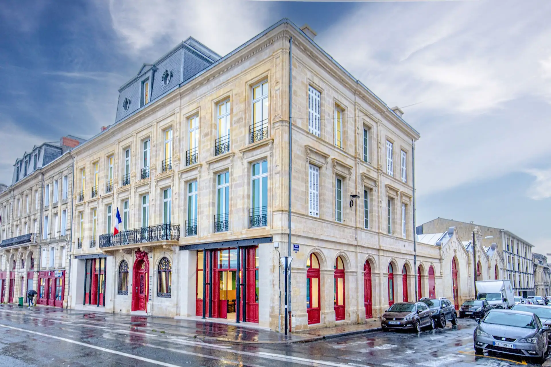 Restored honey-stone facade of the Queyries project in Bordeaux, with red joinery on the ground floor